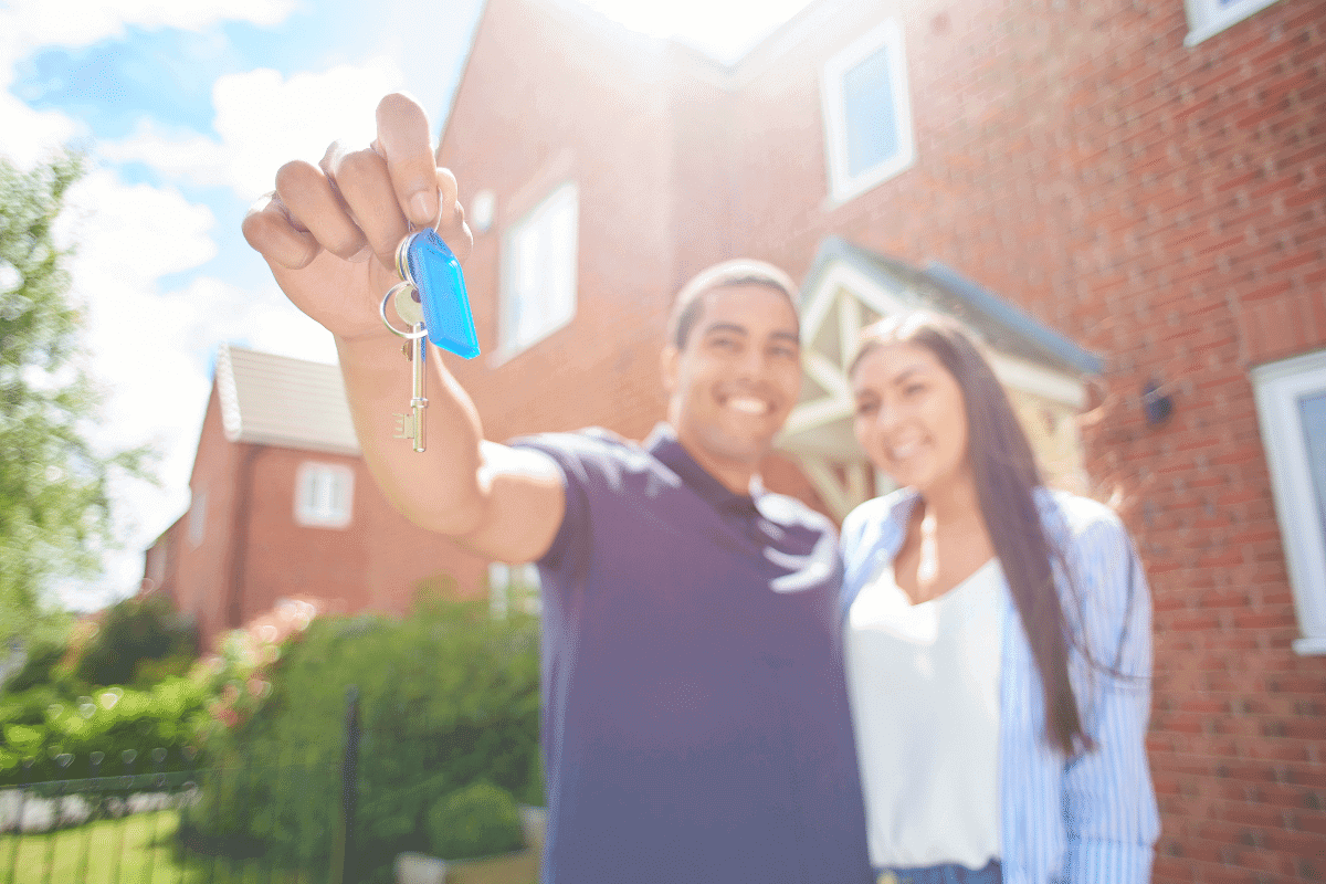 young couple holding the key outside of their new brick home